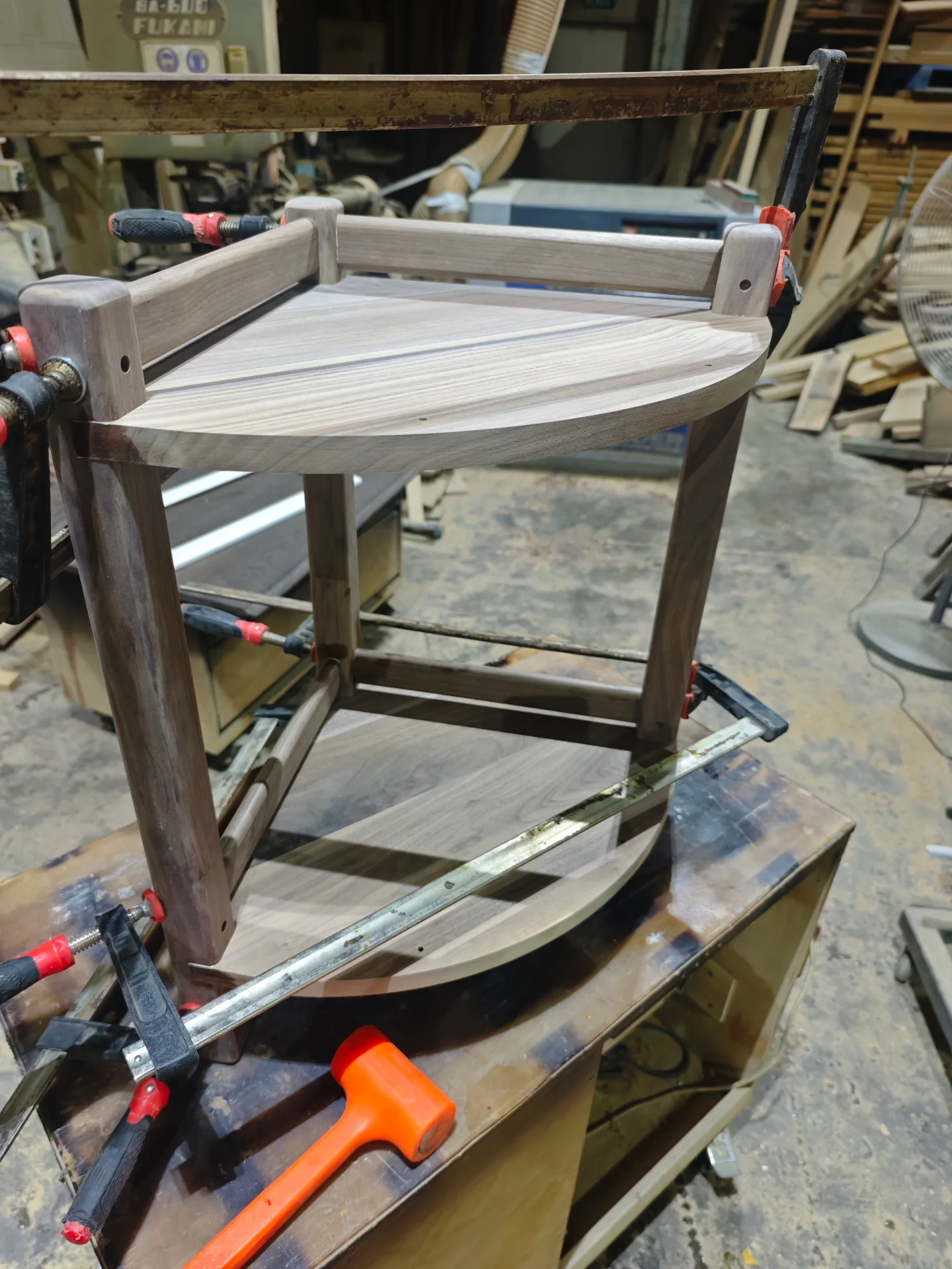 Curved walnut shelf and frame held in clamps on the bench